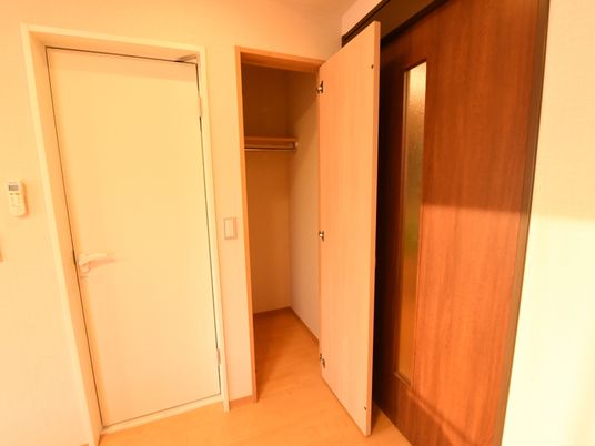 白い扉と茶色い扉のあいだには奥行きのあるウォークインクローゼットがある。ハンガー掛けの上には棚がある。
