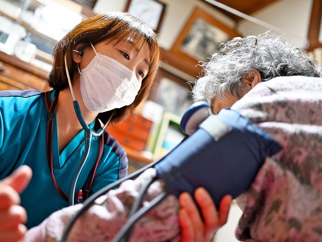 介護スタッフと利用者のふれあい 機能訓練室 優しい表情で利用者の方の血圧を測定するスタッフの姿。ゆったりとした時間が流れる空間です。