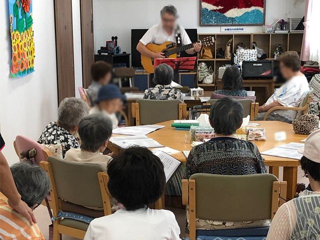 和やかな集いの場 リビング リラックスした雰囲気の中で音楽の演奏が行われ、他の方々が楽しんでいる様子です。参加者の交流を楽しめる空間となっています。