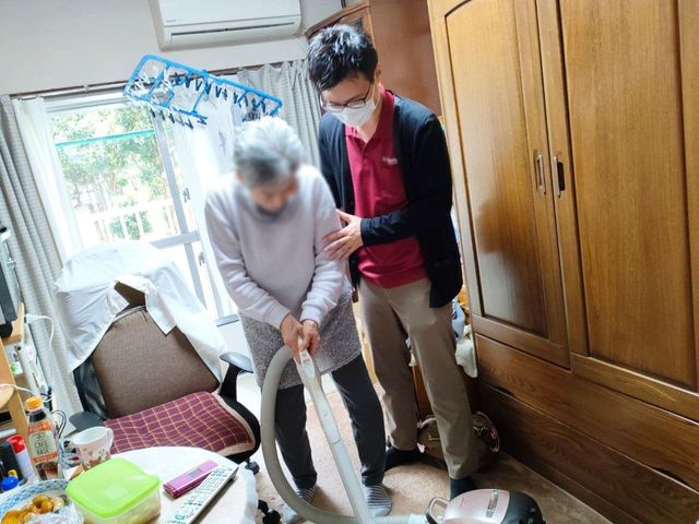 高齢者の支援場面 居室 自然光が差し込む居室で、スタッフが高齢者を丁寧にサポートしています。居心地よさが伝わります。
