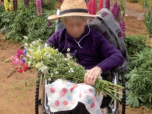 庭で花を楽しむ利用者 庭園 自然に囲まれた環境で、利用者が花と触れ合う穏やかなひと時を体感できます。車椅子でも安心して庭園をお楽しみいただける設計になっています。
