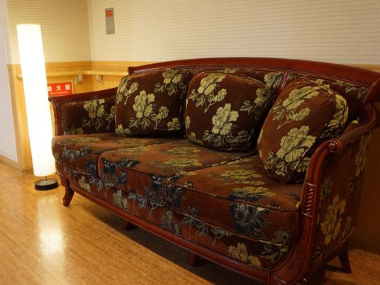 木製の重厚感のあるソファーである。奥には縦型の間接照明が設置されており、入居者様の談笑などに使用することができる。