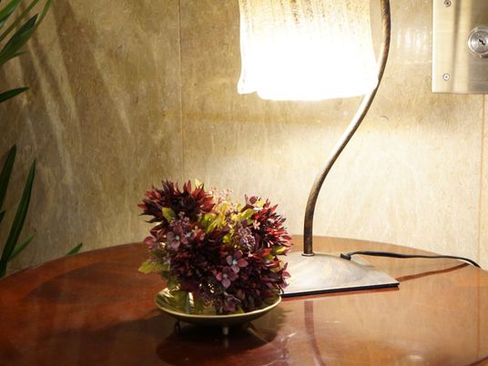 ダークブランの木製のテーブルの上にシックな色合いの花がセンスよく飾られている。ガラス製のスタンドが置かれている。