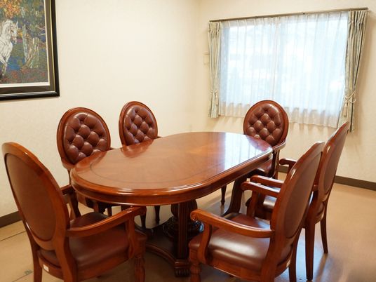 高級感がある楕円形の木製のテーブルと、革張りの椅子が6脚置かれている談話室。壁には絵画が飾られている。