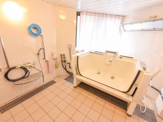 介助付きで座った状態から入浴できる浴槽が付いている。左手にシャワーが付いており、その横にナースコールのオレンジ色のボタンがある。