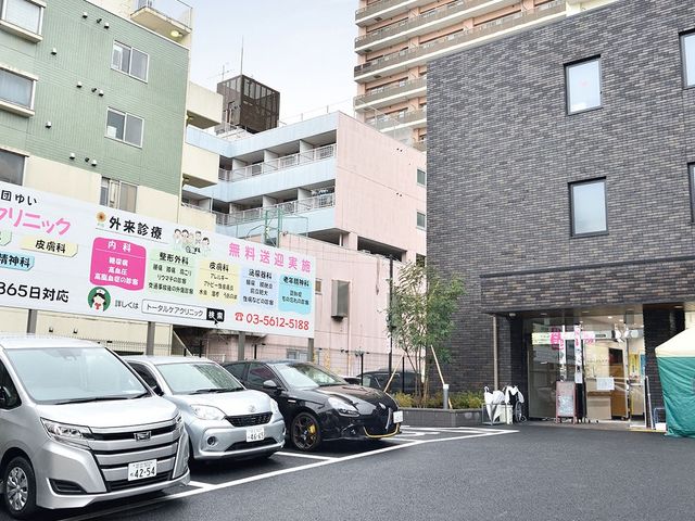 建物正面の駐車場 外観   建物前に駐車スペースがあり、出入りしやすい印象です。周辺は高層住宅に囲まれた都市部の立地です。
