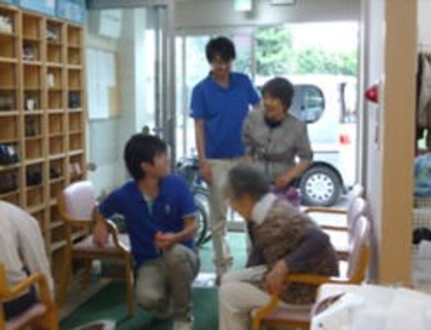 ケアの様子 中庭 多目的室 スタッフが笑顔で対応し、利用者と身体機能向上のための活動を行っている様子です。明るくゆったりとした空間が特徴です。