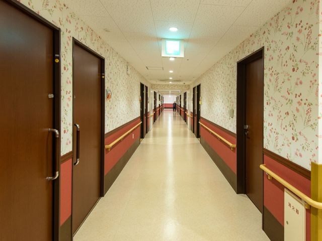 廊下の清潔な長い通路 廊下 ゆったりとした廊下は清潔感に溢れ、壁には柔らかな色彩の花柄が配されています。手すりも設置され、安心して歩ける環境です。