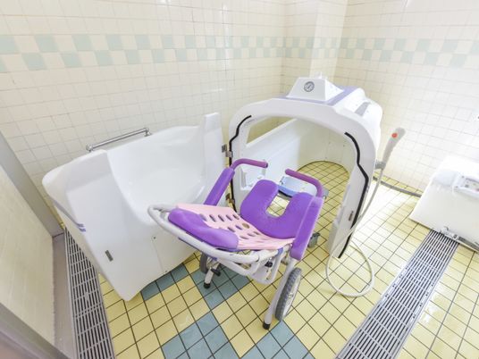 入浴をサポートする椅子は大きなキャスター付きで、U字型の座面、ひじ掛け、枕のクッション部分が紫色になっている。