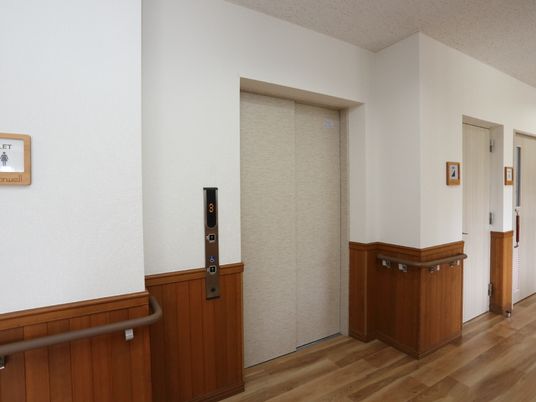 白い壁に木目調の床とのコントラストがモダンな廊下に合わせてエレベーターも白い。車いす専用ボタンがあるので便利。