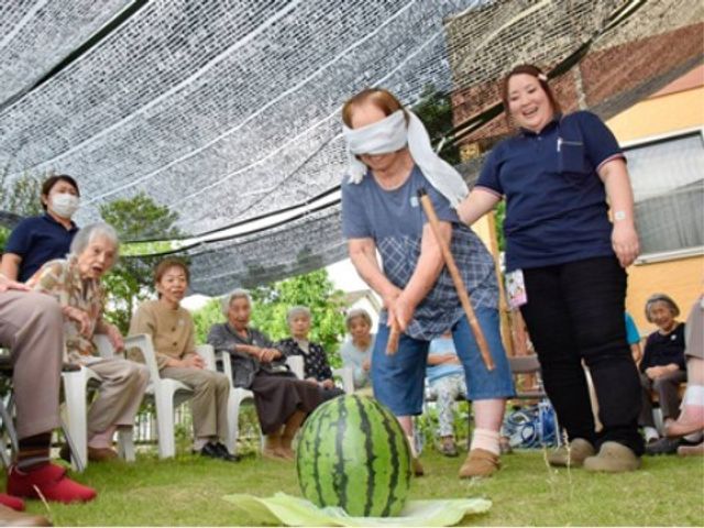 目隠しスイカ割り イベント 目隠しをした方がスイカを割る様子が笑顔で見守られています。共有の庭でのレクリエーションが行われ、心地良いコミュニティを感じられる場です。
