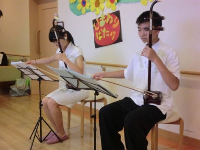 二人で三味線演奏 イベント ケアセンターの明るく開放的な空間で、ご利用者が三味線に触れ、音楽の喜びを分かち合える様子です。音楽を通じて楽しいひと時を提供しています。