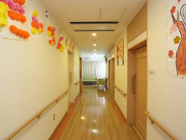 廊下に飾り付けられた空間 リラックスできる談話スペース 壁には手作り感じる装飾があり、木目調の床が温もりを感じさせる廊下です。明るく落ち着いた雰囲気が漂い、訪れる方々を優しく迎え入れます。