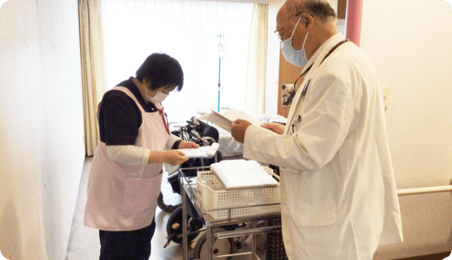 二人のスタッフが話す廊下 廊下   廊下で、医療スタッフが情報を確認し合う様子です。協力し合う姿勢が見られます。