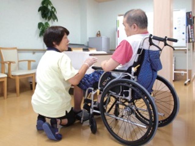 車椅子利用者とスタッフが対話する廊下 廊下 スタッフが親切に対応している様子が印象的です。車椅子の方も安心して過ごせる環境です。