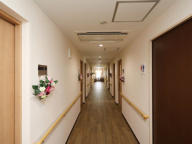 廊下の照明と手すり 廊下 清潔感のある廊下は、手すりが整備されており、安全に配慮された設計です。壁に飾られた花が温かい雰囲気を演出しています。