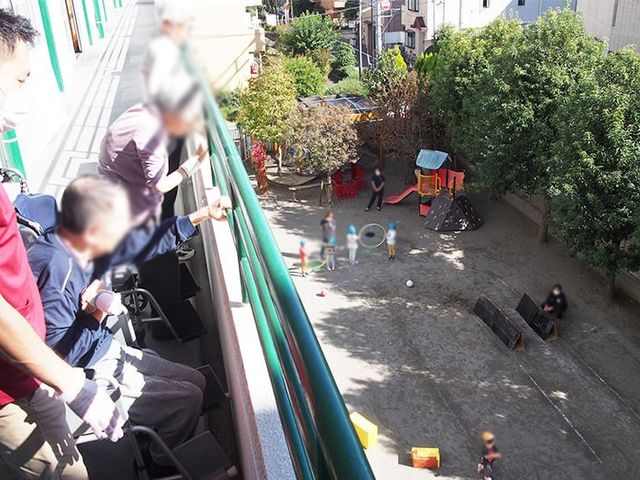 見下ろす中庭の様子 中庭 車椅子に座った方が、陽射しを感じながら中庭の様子を見ています。リラックスできる時間を提供します。