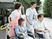 サムネイル 施設の写真 エプロンを付けた若い女性スタッフと男性スタッフが車いすの男女の高齢者に付き添って外出している。