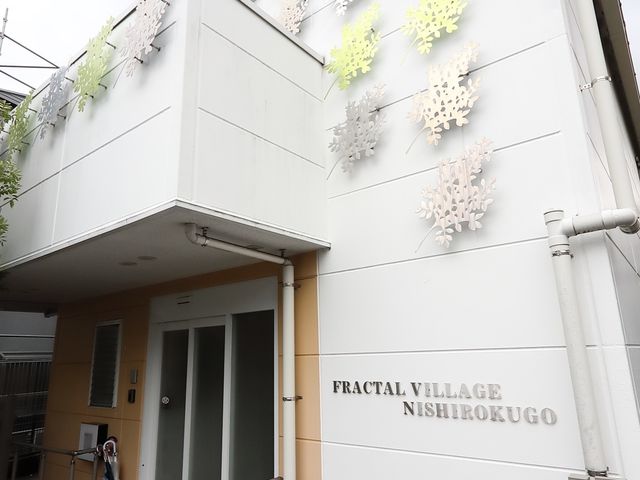 白壁の施設入り口 エントランス 清潔感のあるエントランスに彩り豊かな装飾が施されています。安心してお仕事を始められるような環境です。