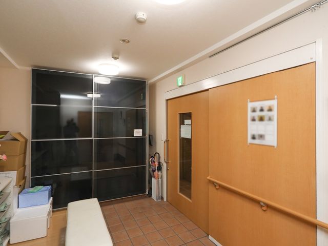 廊下の入口と掲示物 エントランス 明るい照明の下、清潔感のある廊下の様子です。情報を共有する掲示物も見受けられます。