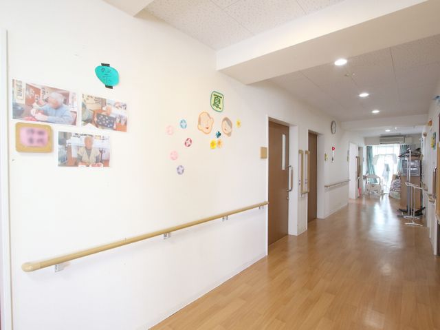 明るい廊下と掲示物 廊下 手すり付きの廊下は、清潔感があり、壁に掲示された写真や装飾がアクセントになっています。明るく広々とした空間は、快適な動線を実現しています。
