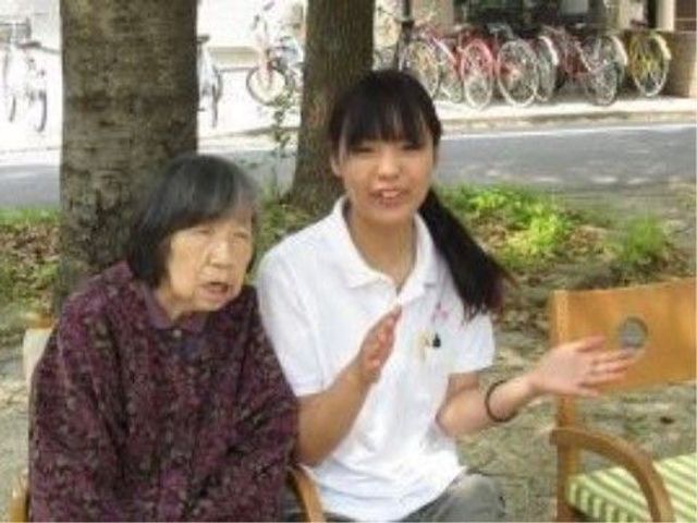 笑顔で話すスタッフと利用者 休憩 明るく穏やかな中庭で、スタッフが笑顔で利用者とお話をしています。快適な環境でのコミュニケーションが売りです。