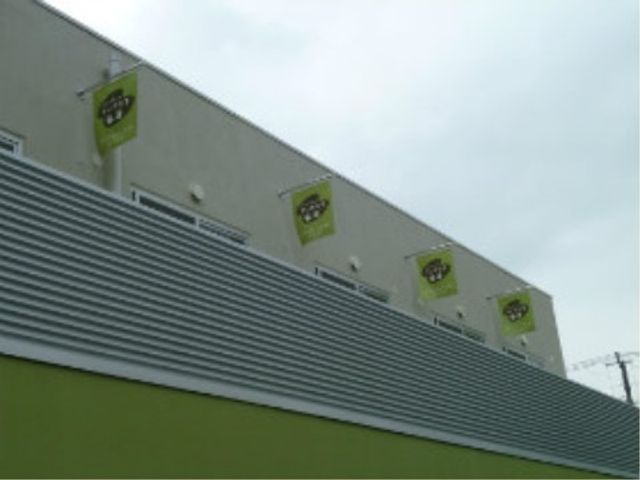 施設のシンボルが並ぶ外観 フラッグ 落ち着いた色彩の外壁が印象的な建物で、清潔感があります。働く環境として、明るい雰囲気を感じられる場所です。