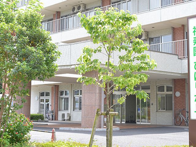 玄関前の看板 看板 施設名が明るく掲示されています。エントランス前には緑があり、雰囲気を和ませます。