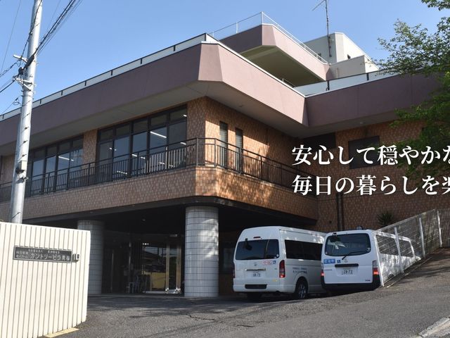 介護施設の外観 外観   落ち着いた色合いの建物外観で、1階部分に車寄せが見えます。玄関前には送迎車が停まっており、通いやすい印象です。
