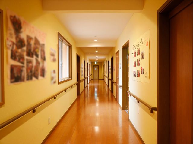 温かみのある廊下の様子 通路 明るい色合いの廊下は、掲示物で生活感が漂い、手すりが安心の歩行を支えます。