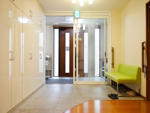 入口付近の明るい空間 玄関 清潔感のあふれるエントランスは、患者様が快適に出入りできるように配慮されています。緑のソファが訪れる方の一時的な休憩スペースとなっています。