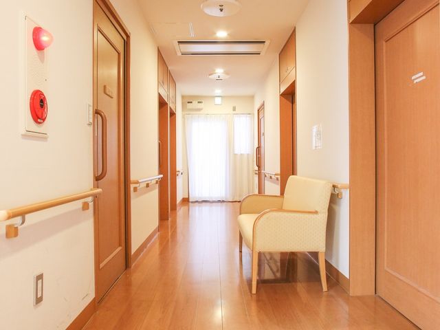 暖かみのある廊下 廊下 手すりが完備された明るい廊下で、安全に快適な移動をサポートしています。木目調の床が温かな印象を与え、落ち着いた雰囲気です。