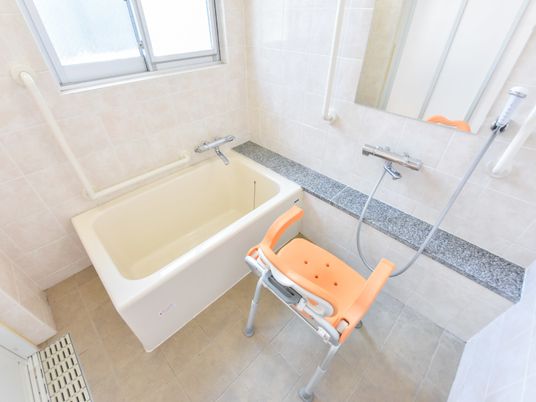 入所者が体を洗いやすいような椅子が設置されている。手すりは、浴槽の近く、鏡の両側といくつか設置されている。