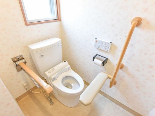 洋式トイレには、通常の手すりの他に、平たい手すり・クッション素材が巻かれた手すりも設置されている。入所者は快適にトイレを利用できる。