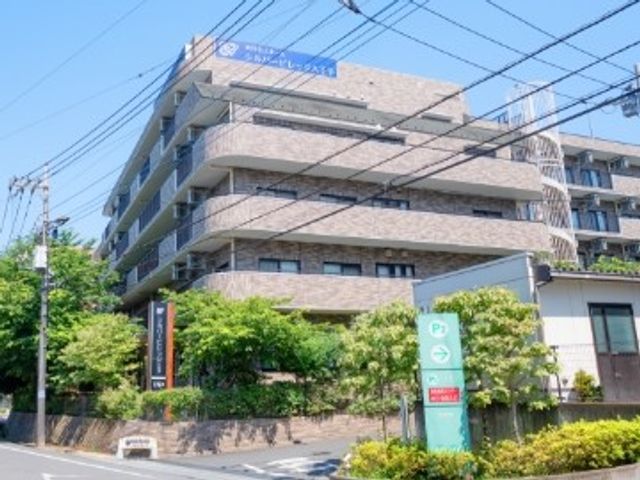 施設の外観 外観   明るい色合いの建物が道路沿いに建ち、植栽が周囲をやわらかく彩っています。就業先の雰囲気を外から確認しやすい外観です。