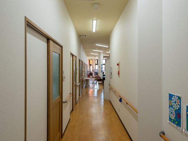 明るい廊下の景観 廊下 ゆとりある廊下には手すりが備わり、奥に座席でくつろぐ方々が見えます。安全で明るい環境が整っており、心地よい時間を過ごせそうです。