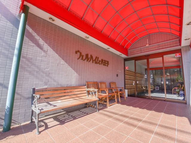 赤い屋根のエントランス 玄関  赤い屋根が印象的なエントランスで、明るく開放的な雰囲気をお感じいただけます。ベンチが設置されており、訪れる方の憩いの場となっています。