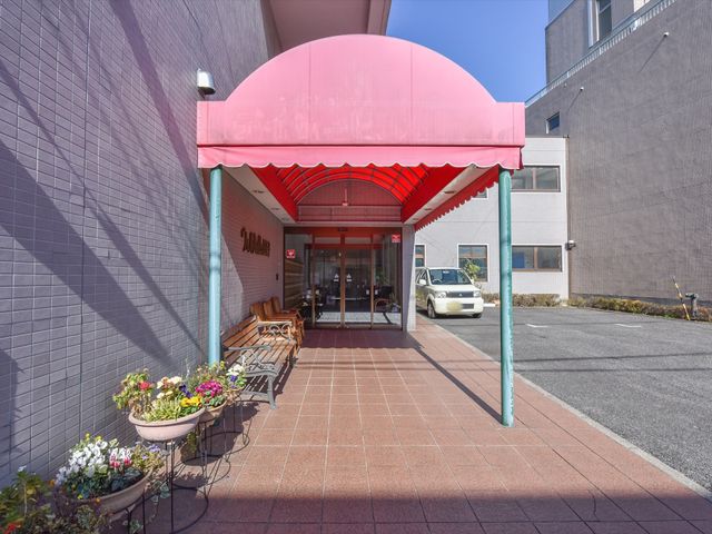 明るいエントランス前景 エントランス  温かみのあるエントランスは訪れる人を優しく迎え入れます。花壇には季節の花が彩りを添え、ベンチがくつろぎの空間を提供しています。