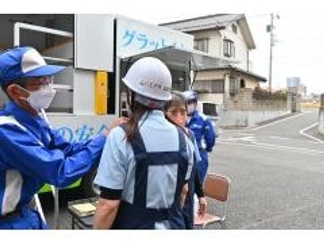 スタッフと利用者の屋外の様子 外観   作業着姿の方々が屋外で集まっており、顔を見ながら声をかけ合っているようです。施設で働く場面を思い描きやすい、落ち着いた雰囲気です。