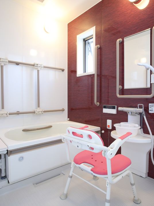 内部に手すりがついた白い浴槽がある。その上部壁に縦横に手すりがある。シャワースペースには鏡があり、ひじ掛け背もたれ付きの椅子がある。
