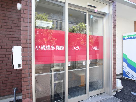 建物から出っ張る形の出入り口である。ガラス戸三枚の扉で施設名が赤色ベースに白字で表示されている。郵便受けがある。