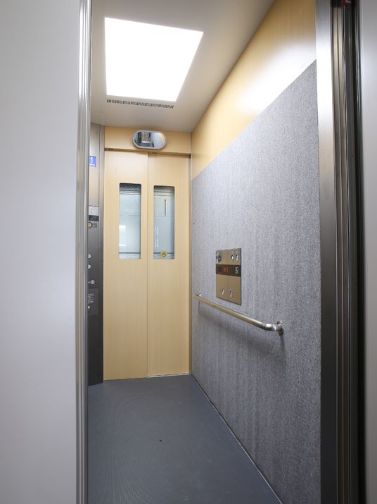 エレベーターは出入り口が2か所ある。内部のスペースは幅は狭いが、奥ゆきがある。出入り口の上部に鏡があり、扉横に操作パネルがある。