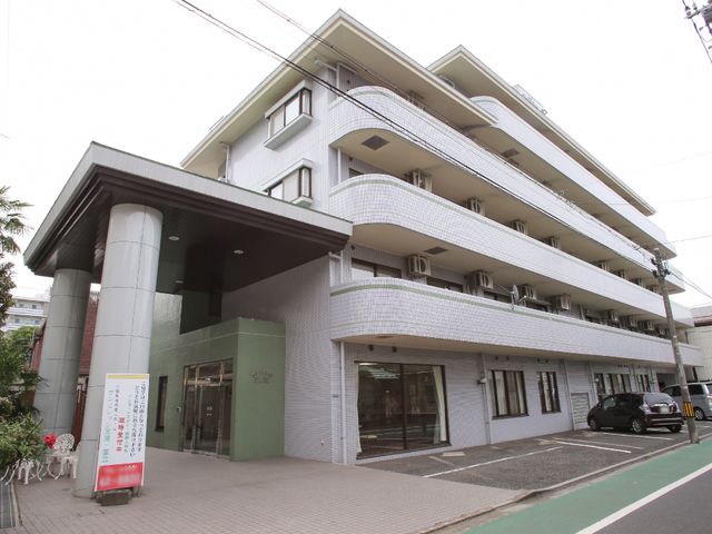 白い建物のエントランス 外観 落ち着いた色合いのエントランスが、訪れる方を優しく迎え入れます。ガラス扉を通して見える明るい軒下スペースが心地よい印象を与えます。