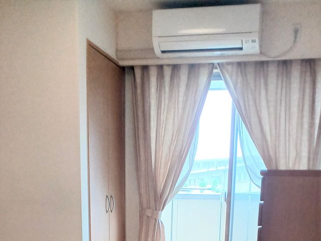 日差し差す居室の窓際 居室   カーテン越しにやわらかな光が入る、落ち着いた居室です。エアコンと収納も見え、働く場面をイメージしやすい空間です。