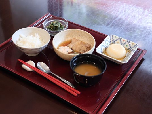 お盆の上には主食のご飯、汁物の味噌汁、そのほかに鳥の煮物やほうれんそうのごま和え、デザートが乗っている。
