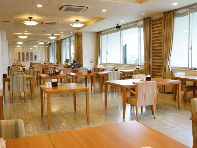 広々した明るい食堂 レストラン ゆったりとしたテーブル配置で、明るい窓辺には２人の方がくつろいでいます。ここでの食事は、毎日の楽しみの一つになることでしょう。