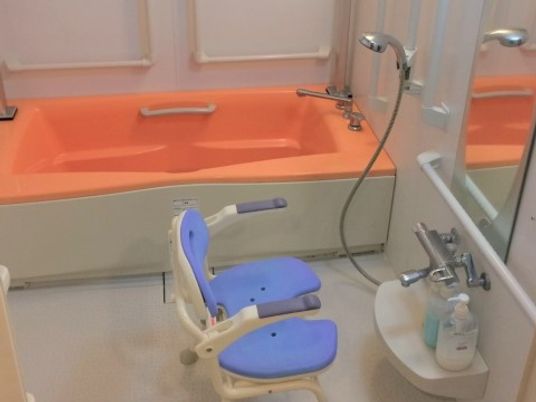 シャワー脇やオレンジ色の浴槽付近には、手すりを取り付けている。シャワー前には、介護用のシャワー椅子が置かれている。