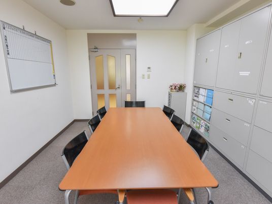 相談室には、１台のテーブルに８脚の椅子が配備されている。壁には、書類棚やホワイトボードが設置されている。
