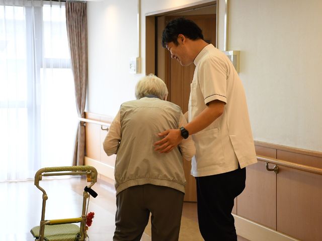 スタッフと利用者の支援シーン 個別リハビリ スタッフが優しく利用者を支えており、安全に歩行訓練を行っています。