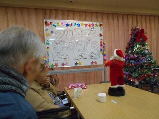 飾り付けされたホワイトボードに、イベント内容が書かれてある。となりに大きなクリスマスツリー、テーブルの上にはサンタ人形が飾られている。
